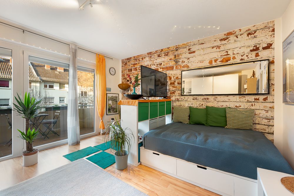 Wohnzimmer mit Balkon, großem Fenster, Tagesbett und Backsteinwand.