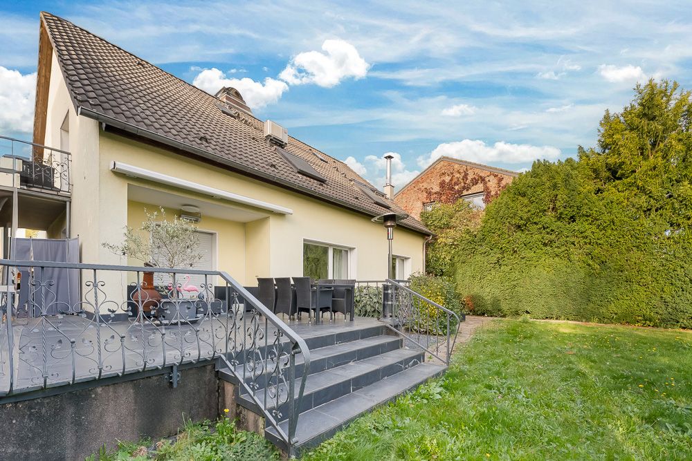 Ein Einfamilienhaus mit großer Terrasse, Garten und Rasenfläche im Vordergrund.