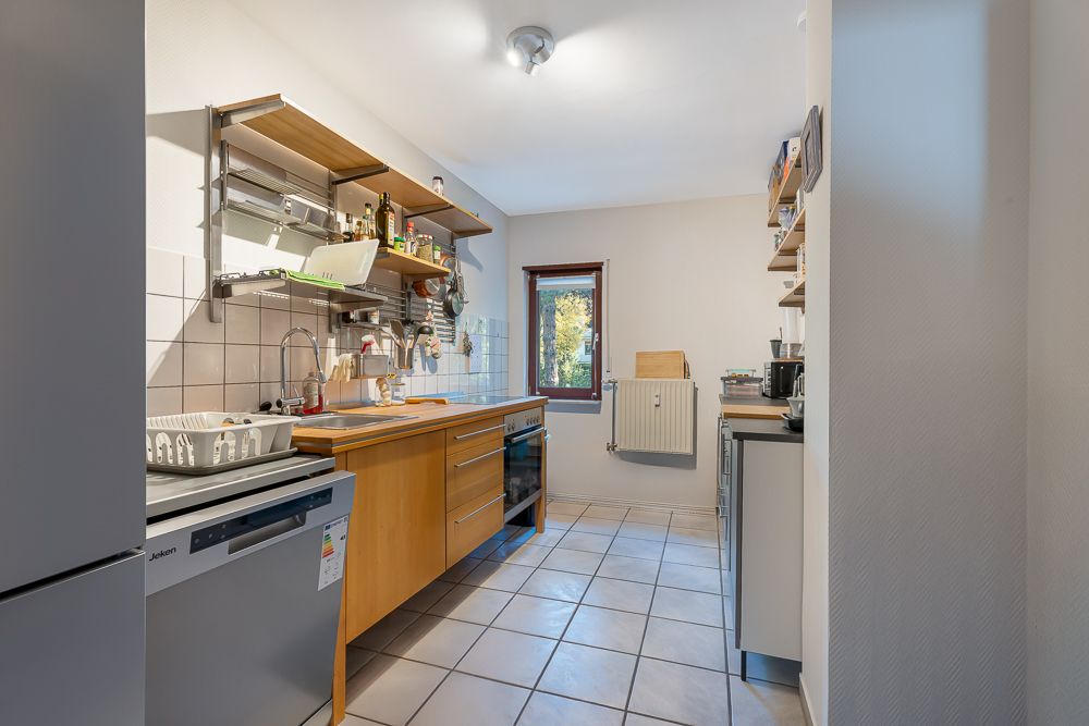 Helle Küche mit Holzarbeitsplatte, offenen Regalen, Fenster und weißen Fliesen.