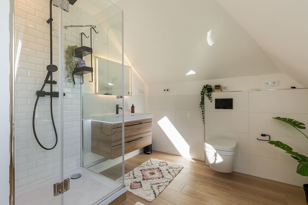 Modernes Badezimmer mit Dusche, Waschtisch, Toilette, Pflanzen und Teppich auf Holzfußboden.