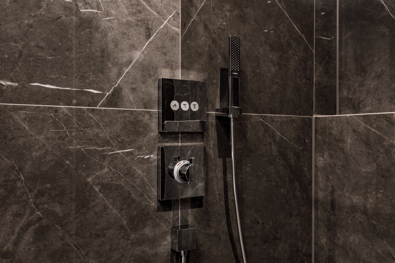 Duscharmatur und Handbrause vor dunklen Marmorfliesen in einer Dusche.