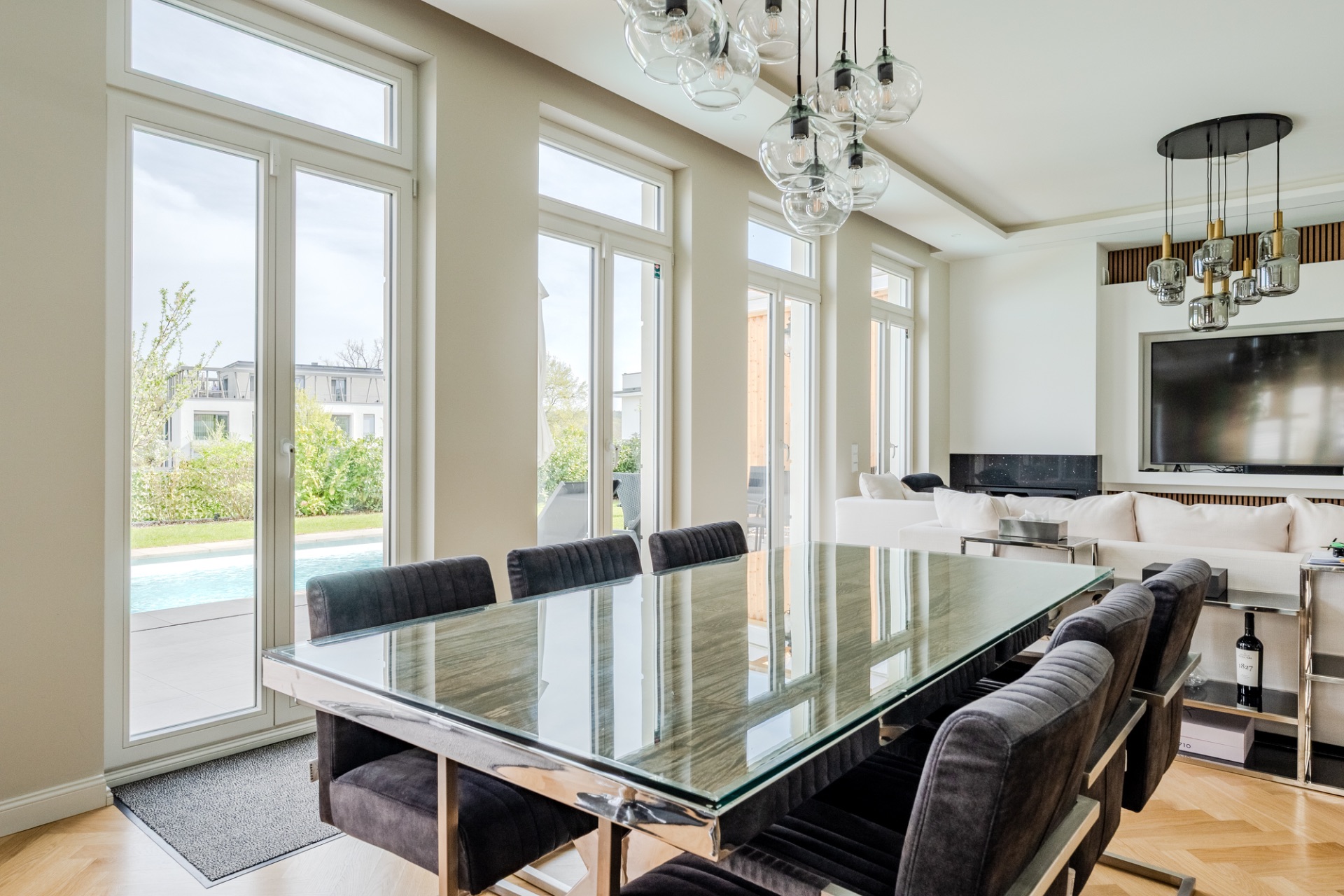 Moderner Essbereich mit Glastisch und schwarzen Stühlen, große Fenster zeigen Garten und Pool.