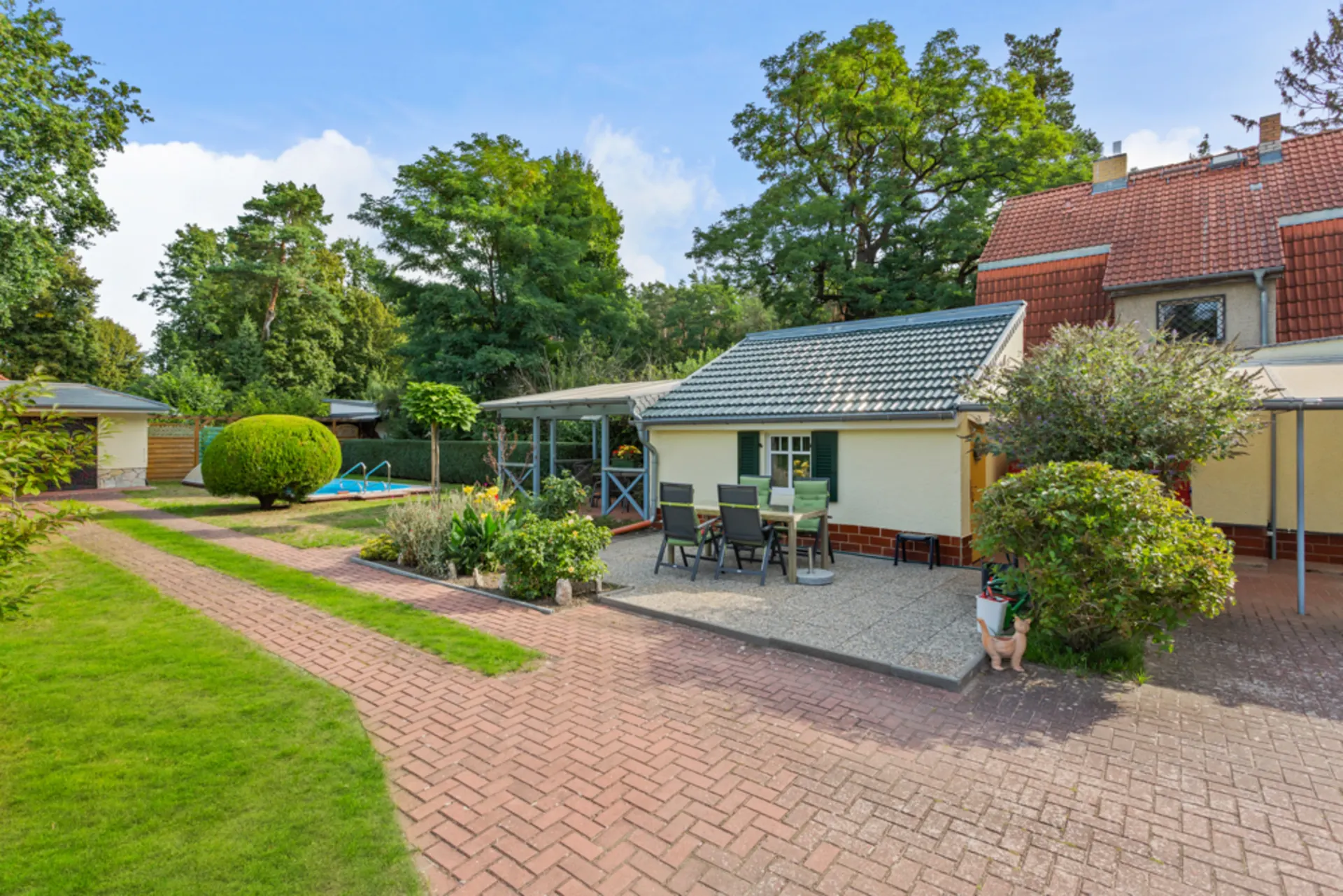 Gepflegter Garten mit Terrasse, Sitzgruppe und kleinem Haus im Grünen.