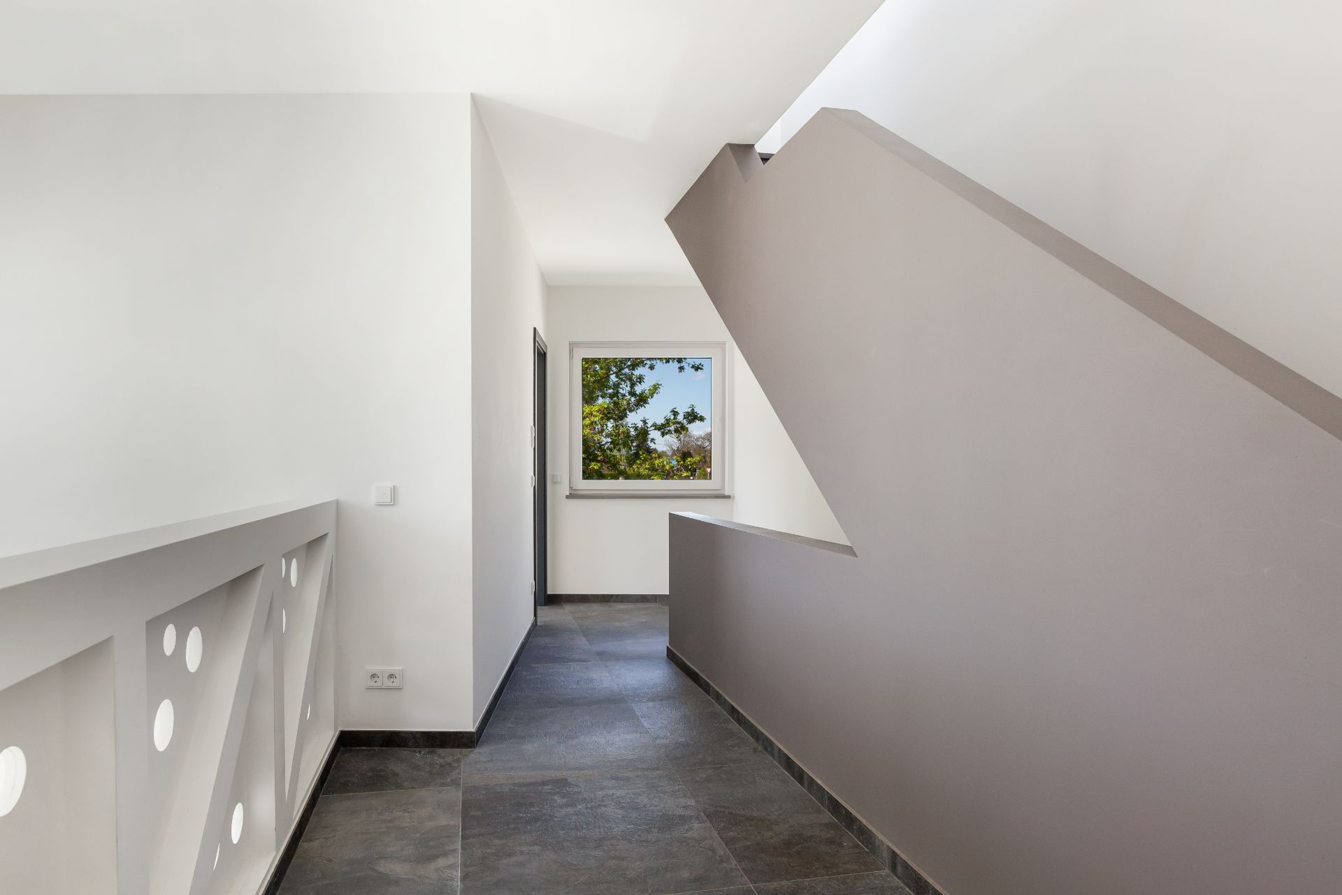 Heller Flur mit Treppe, Fenster am Ende und modernen Geländern.