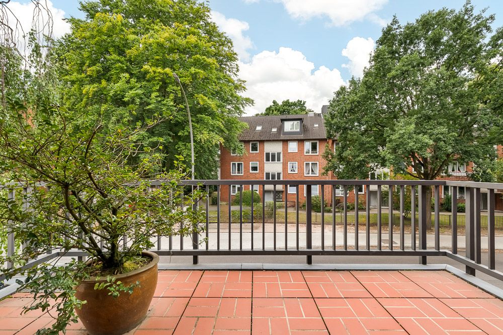 Geräumiger Balkon mit Terrakottafliesen, Pflanze im Topf und Blick auf Wohnhäuser mit Bäumen.