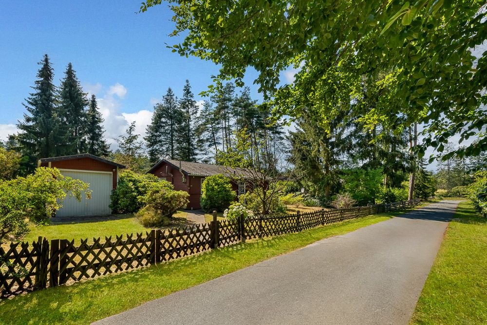 Wohnhaus mit Garten, Holzzaun und Einfahrt, von Bäumen und Sträuchern umgeben.