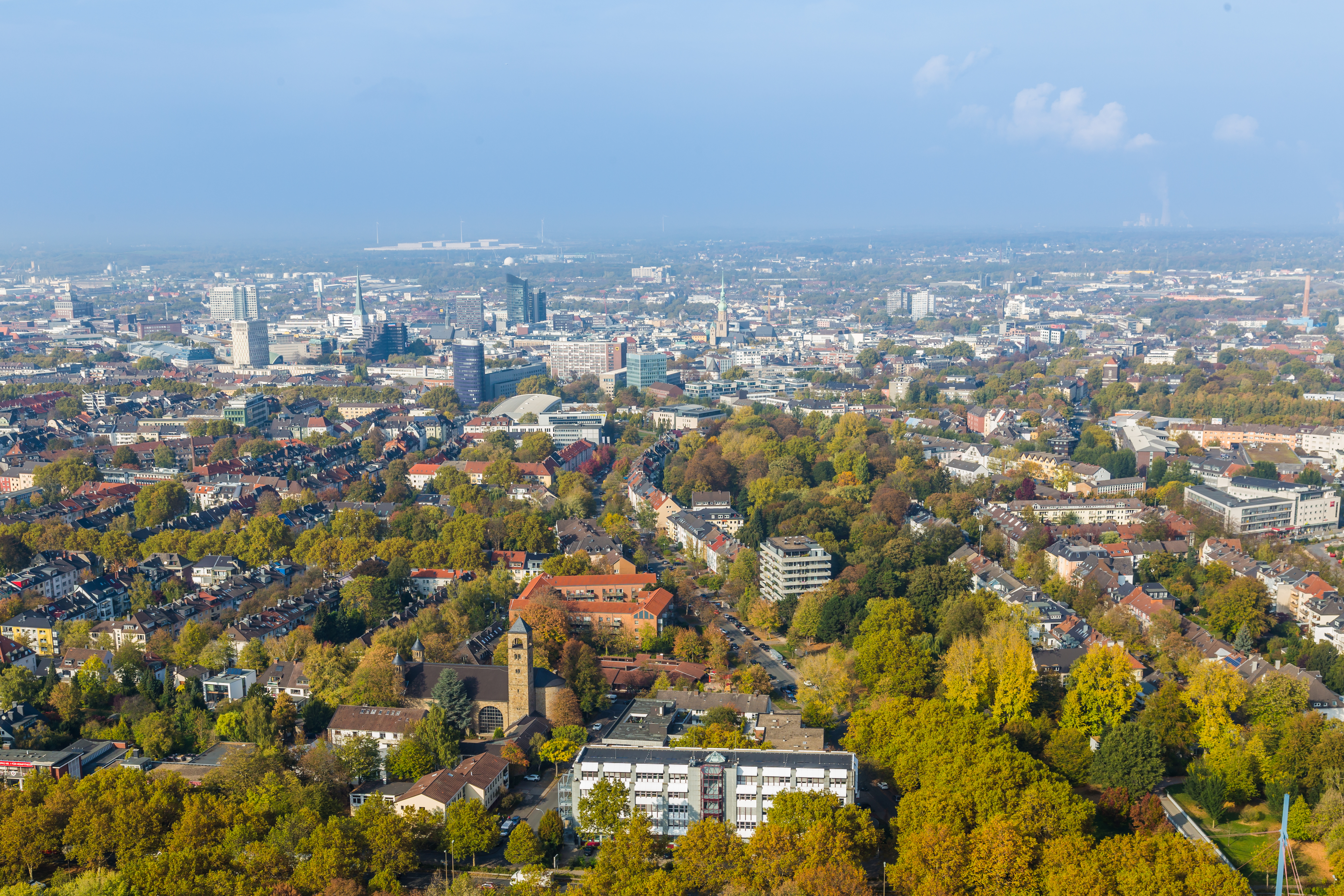 Luftaufnahme einer Stadt mit vielen Bäumen und Wohnhäusern bei klarem Himmel.