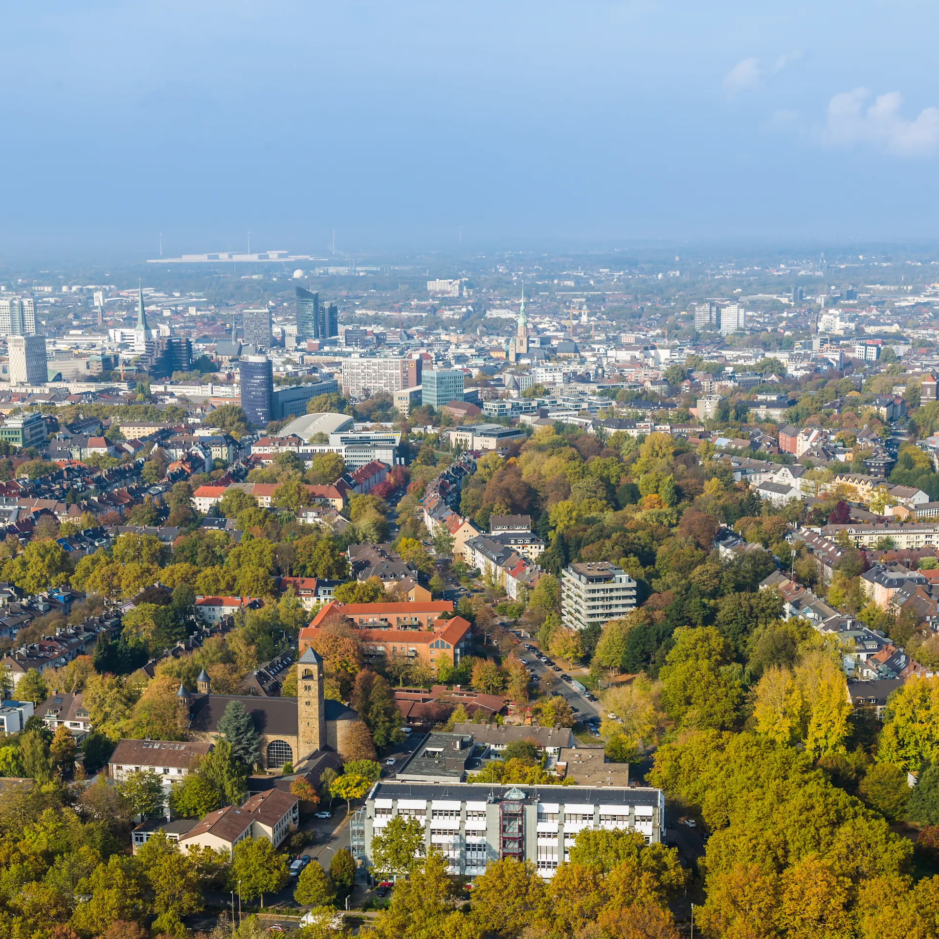 Luftaufnahme einer Stadt mit vielen Bäumen und Wohnhäusern bei klarem Himmel.