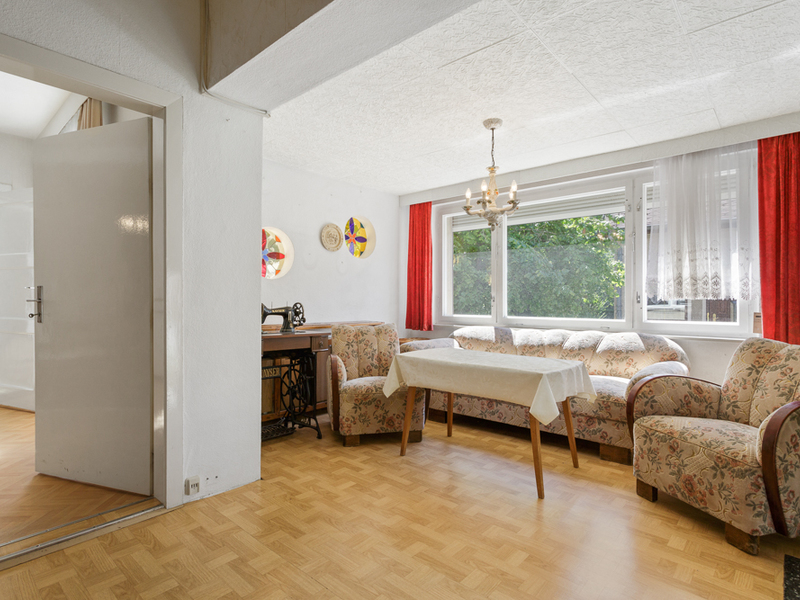 Wohnzimmer mit floralen Polstermöbeln, Esstisch, großer Fensterfront und rotem Vorhang.