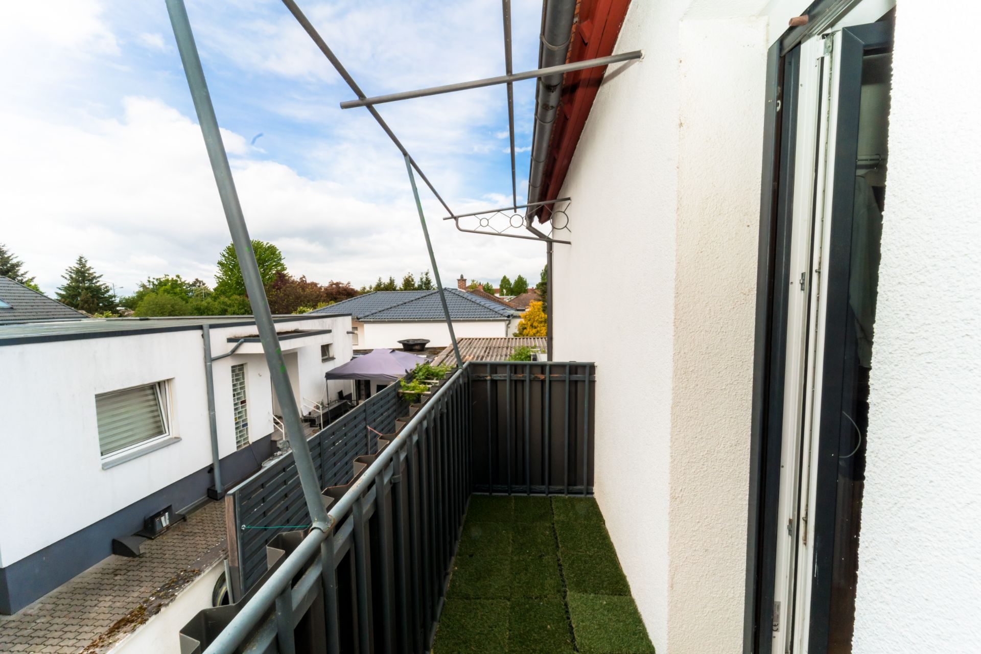 Schmaler Balkon mit Kunstrasenboden, Geländer und Blick auf Nachbarhäuser.