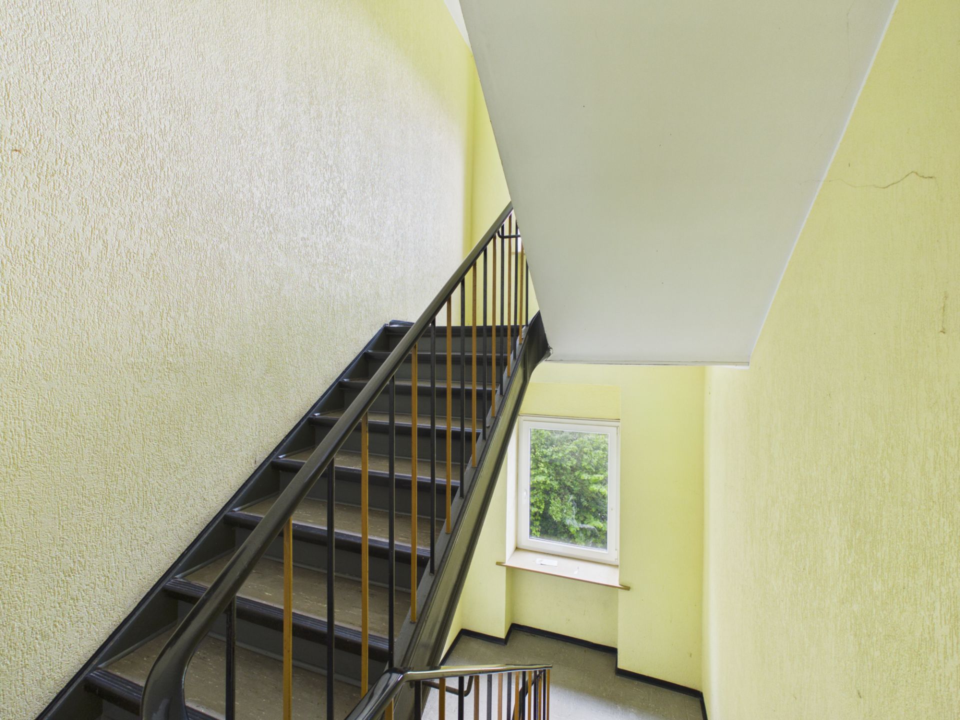 Treppenhaus mit Geländer und Fenster, Wände in hellem Gelb gestrichen.