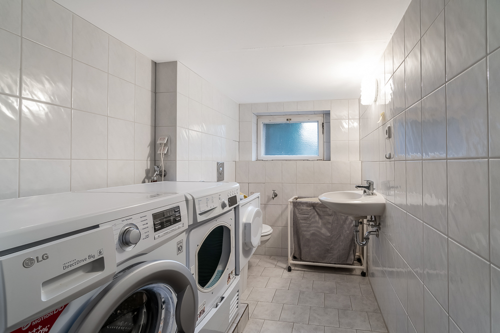 Gefliester Hauswirtschaftsraum mit Waschmaschine, Trockner, Waschbecken und Fenster.