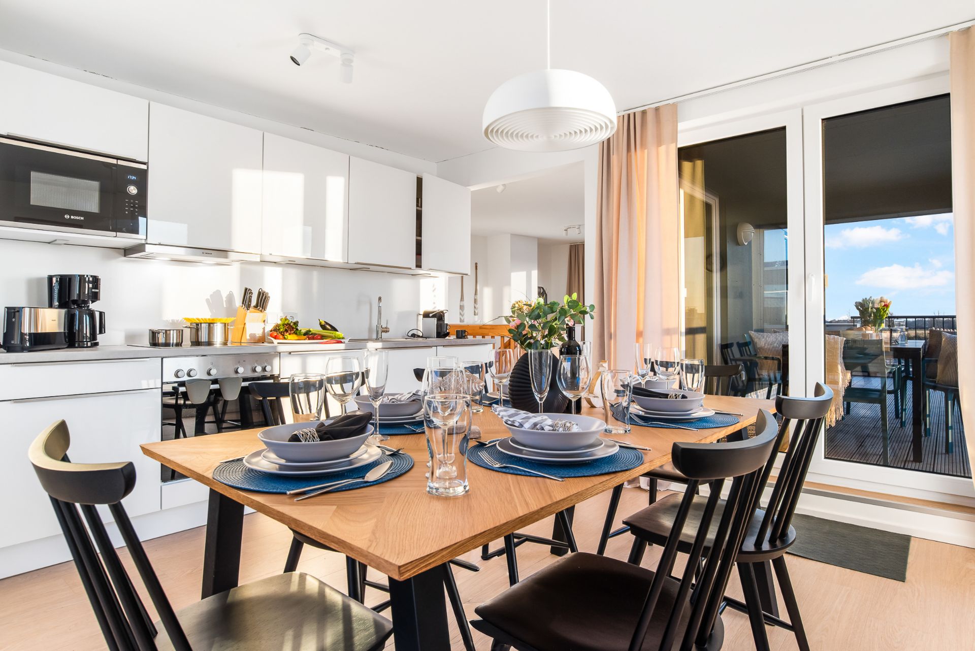 Moderne Küche mit Essbereich, gedecktem Holztisch und großen Fenstern zu einem Balkon.