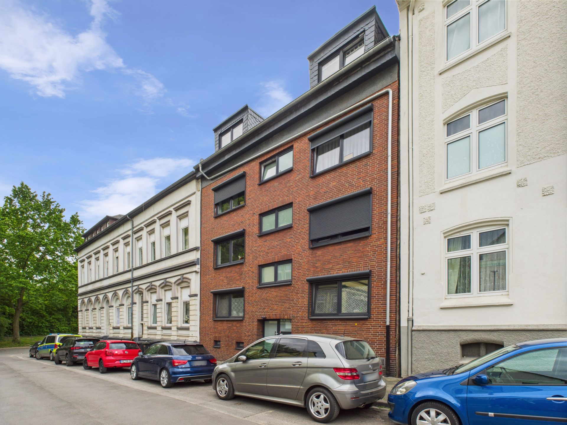 Mehrfamilienhaus mit roter Backsteinfassade und parkenden Autos davor.