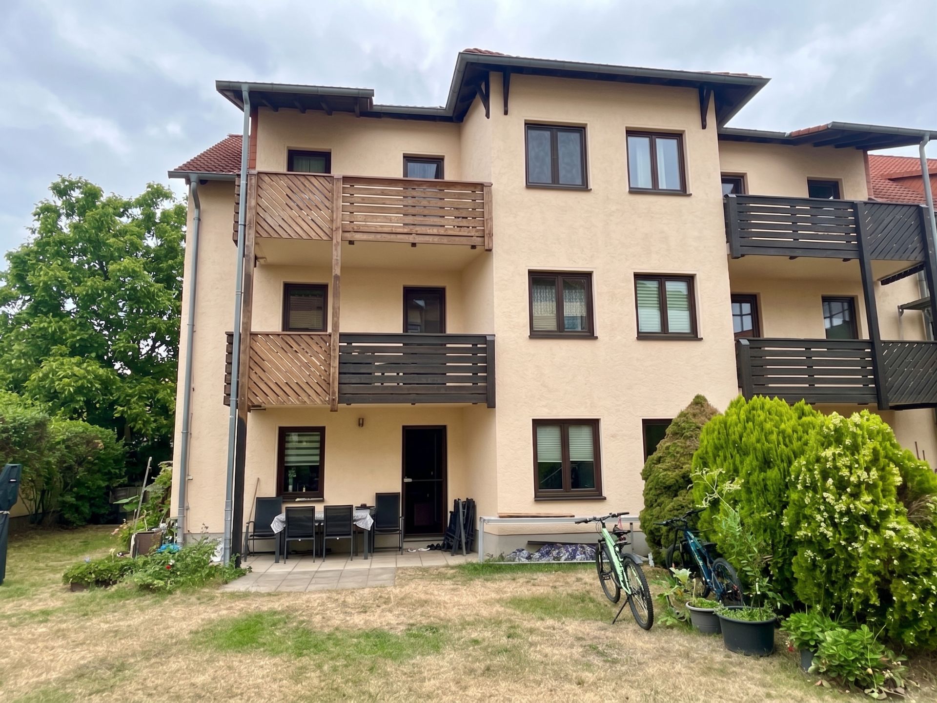 Dreistöckiges Wohnhaus mit Balkonen, Terrasse und Garten mit Fahrrädern und Pflanzen.