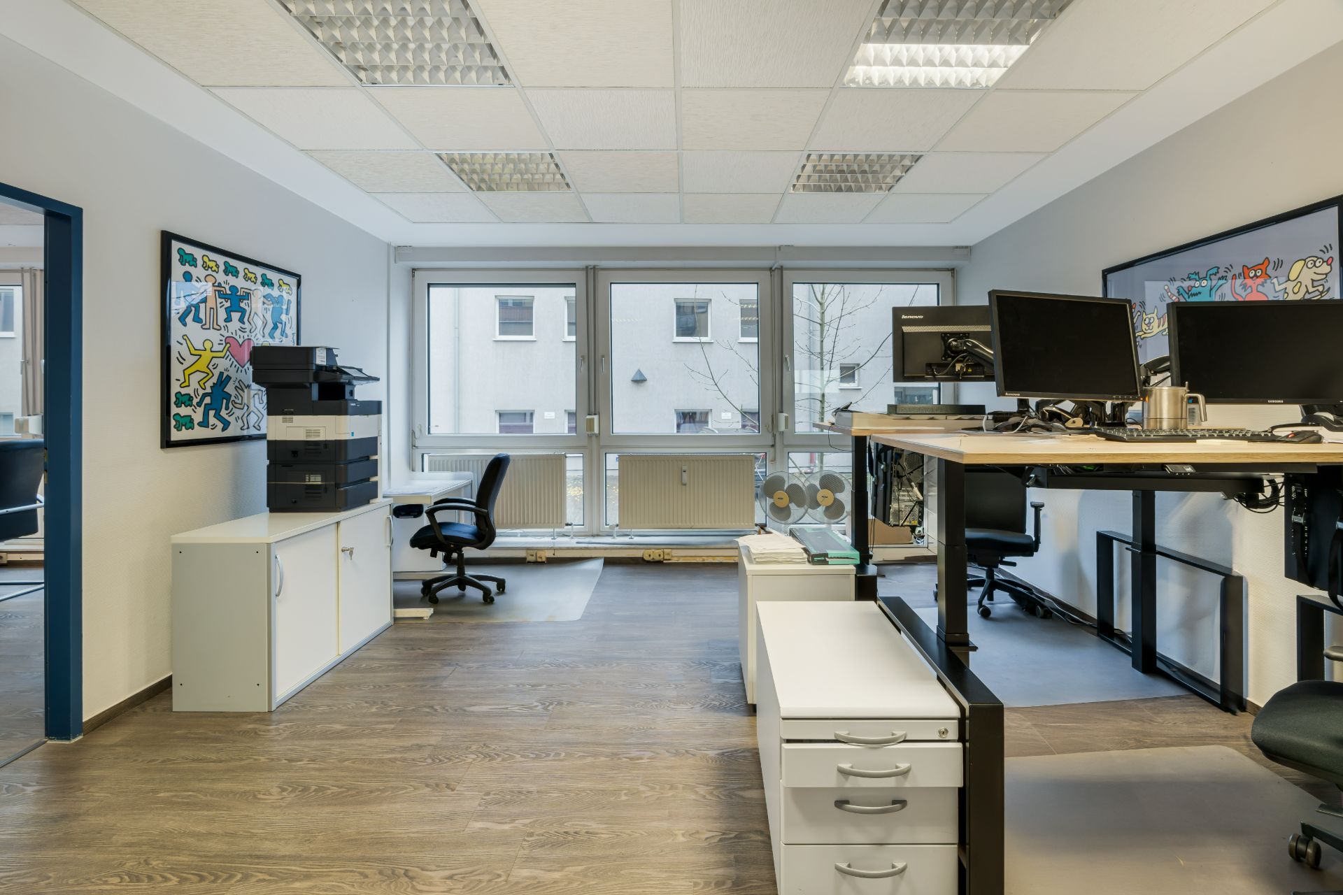 Modernes Arbeitszimmer mit Schreibtischen, Bürostühlen und großen Fenstern.