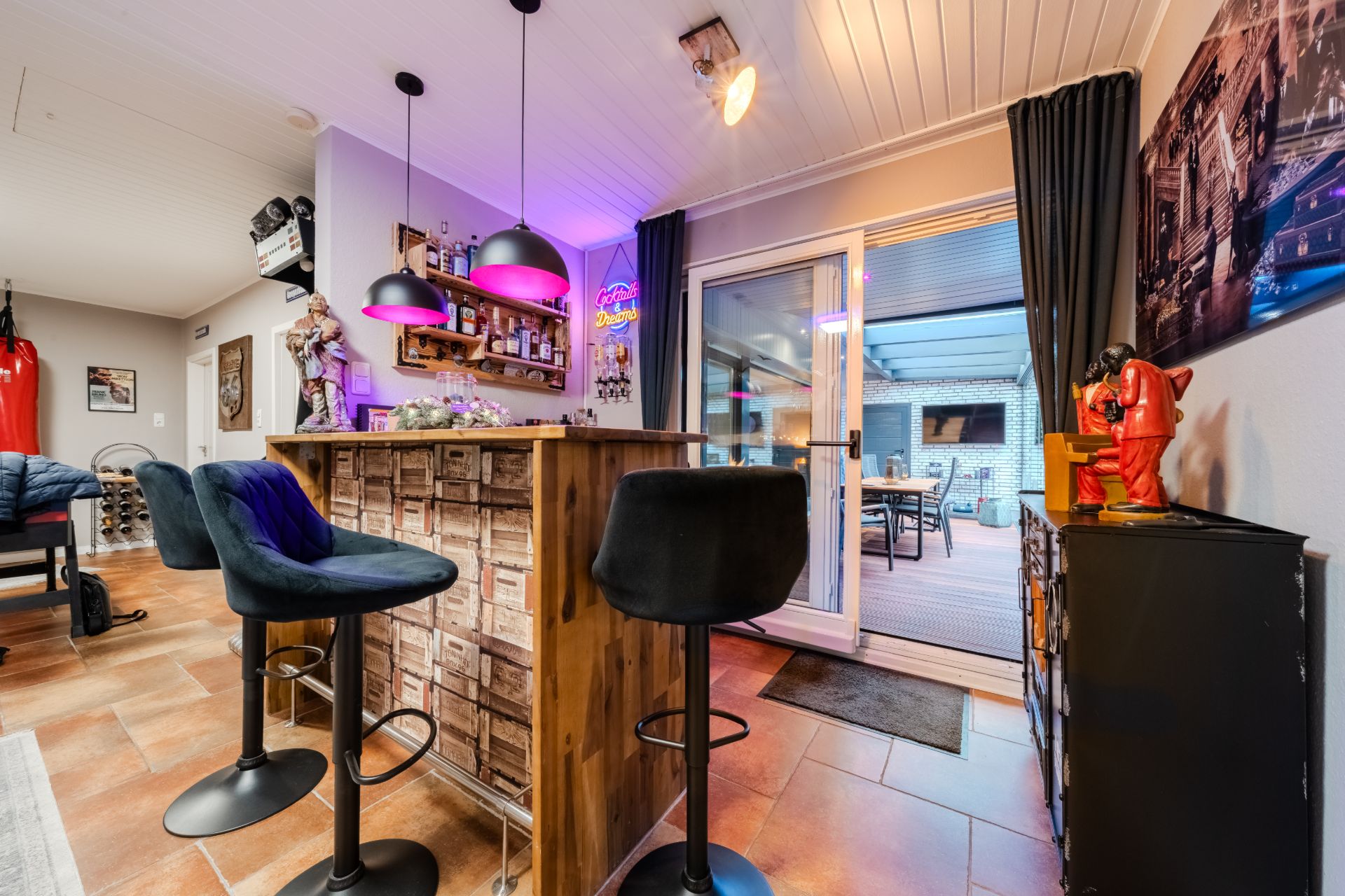 Moderne Hausbar mit drei Barhockern, Regal mit Flaschen und bunter Beleuchtung, Blick auf Terrasse.