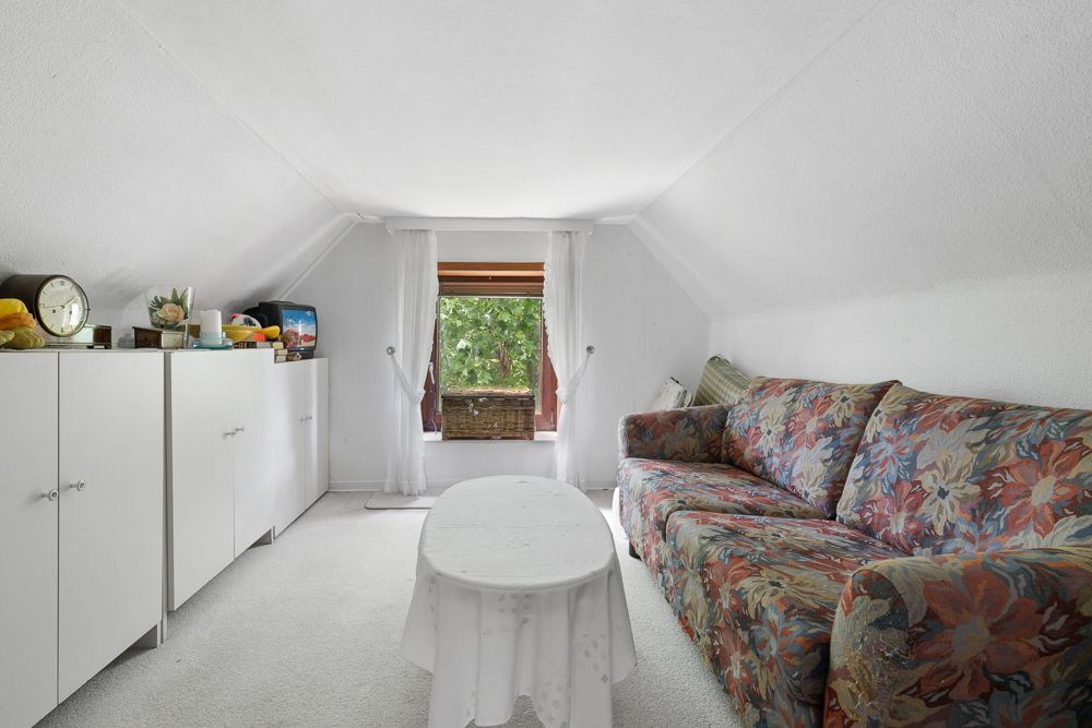 Kleines Wohnzimmer mit bunter Couch, weißem Tisch und Fenster mit Blick ins Grüne.