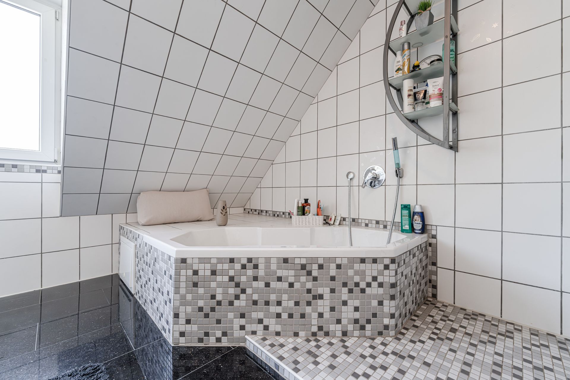 Modernes Badezimmer mit Eckbadewanne, schräger Decke, Mosaikfliesen und Wandregal.