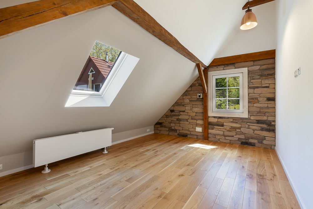 Dachzimmer mit Holzfußboden, Dachfenster, sichtbaren Balken und Steinwand.