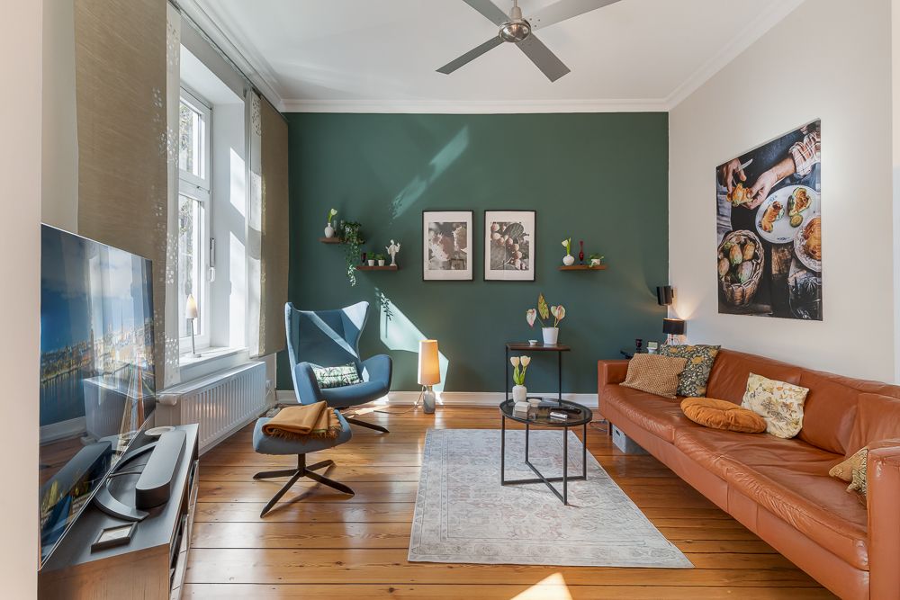 Helles Wohnzimmer mit Ledersofa, Sessel, Teppich und Wanddeko, Holzboden und grüne Akzentwand.