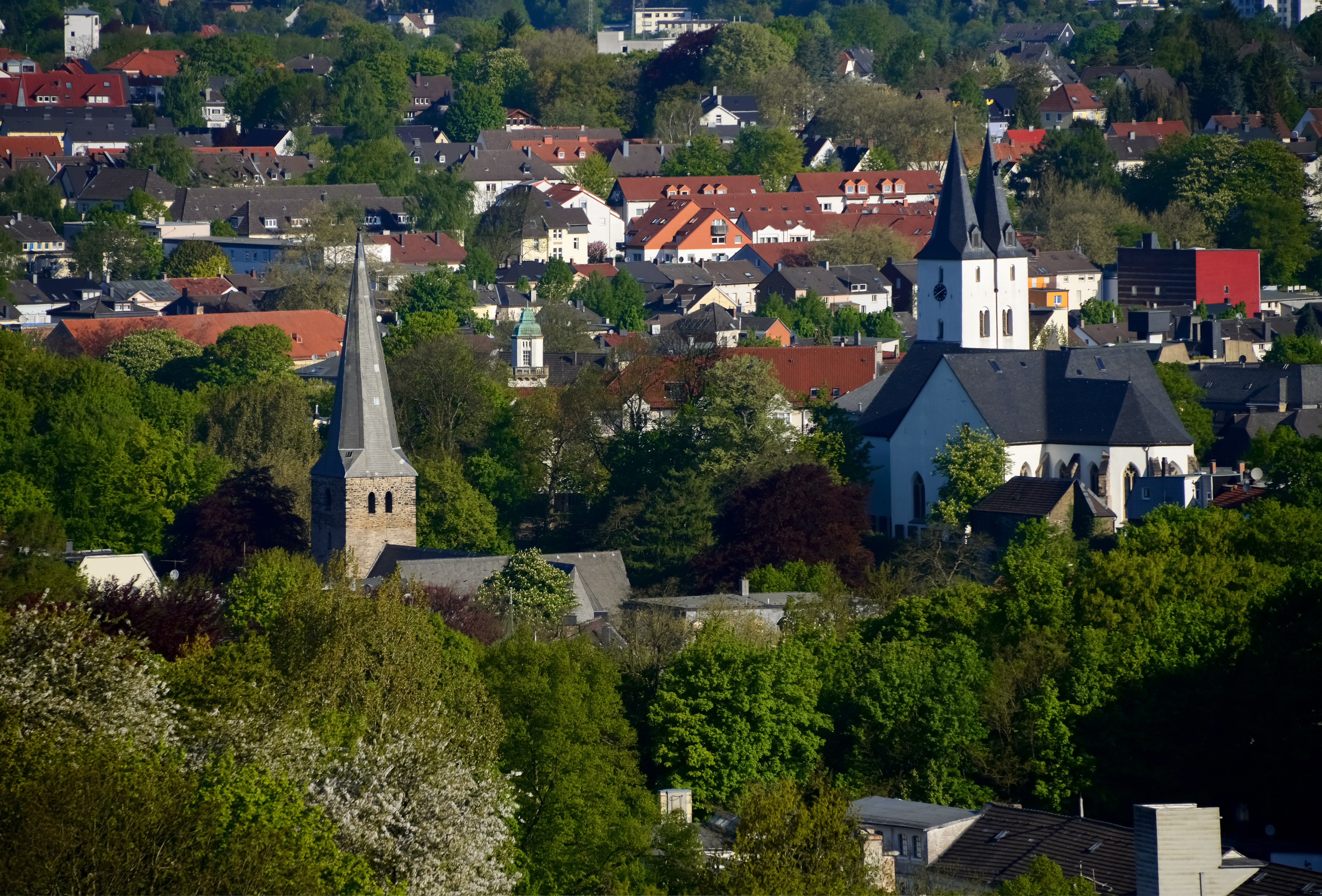 Stadtansicht mit vielen Wohnhäusern, Bäumen und zwei Kirchen mit Türmen.