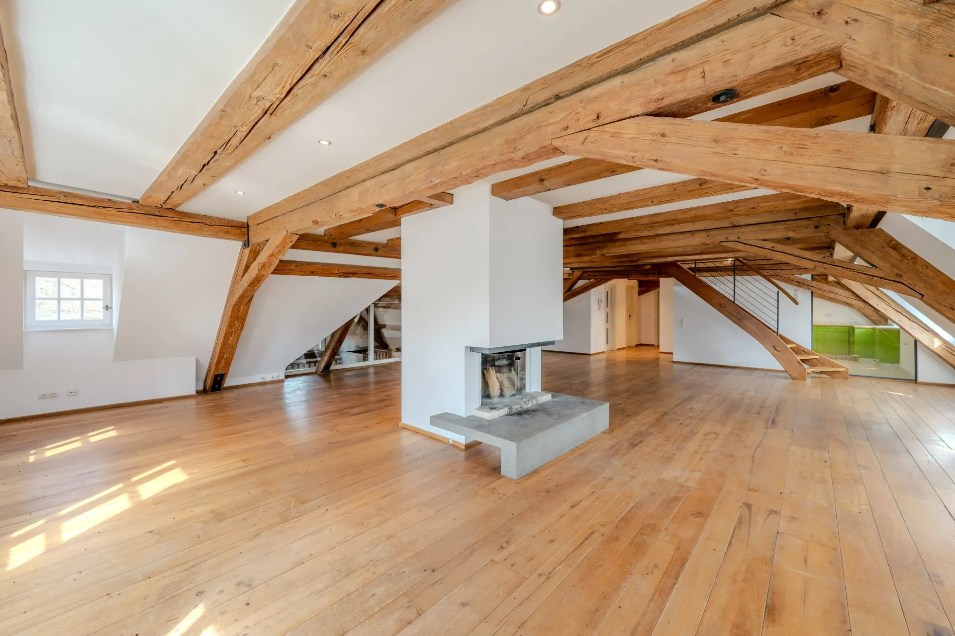 Großer Dachraum mit Holzbalken, Holzfußboden und modernem Kamin in der Mitte.