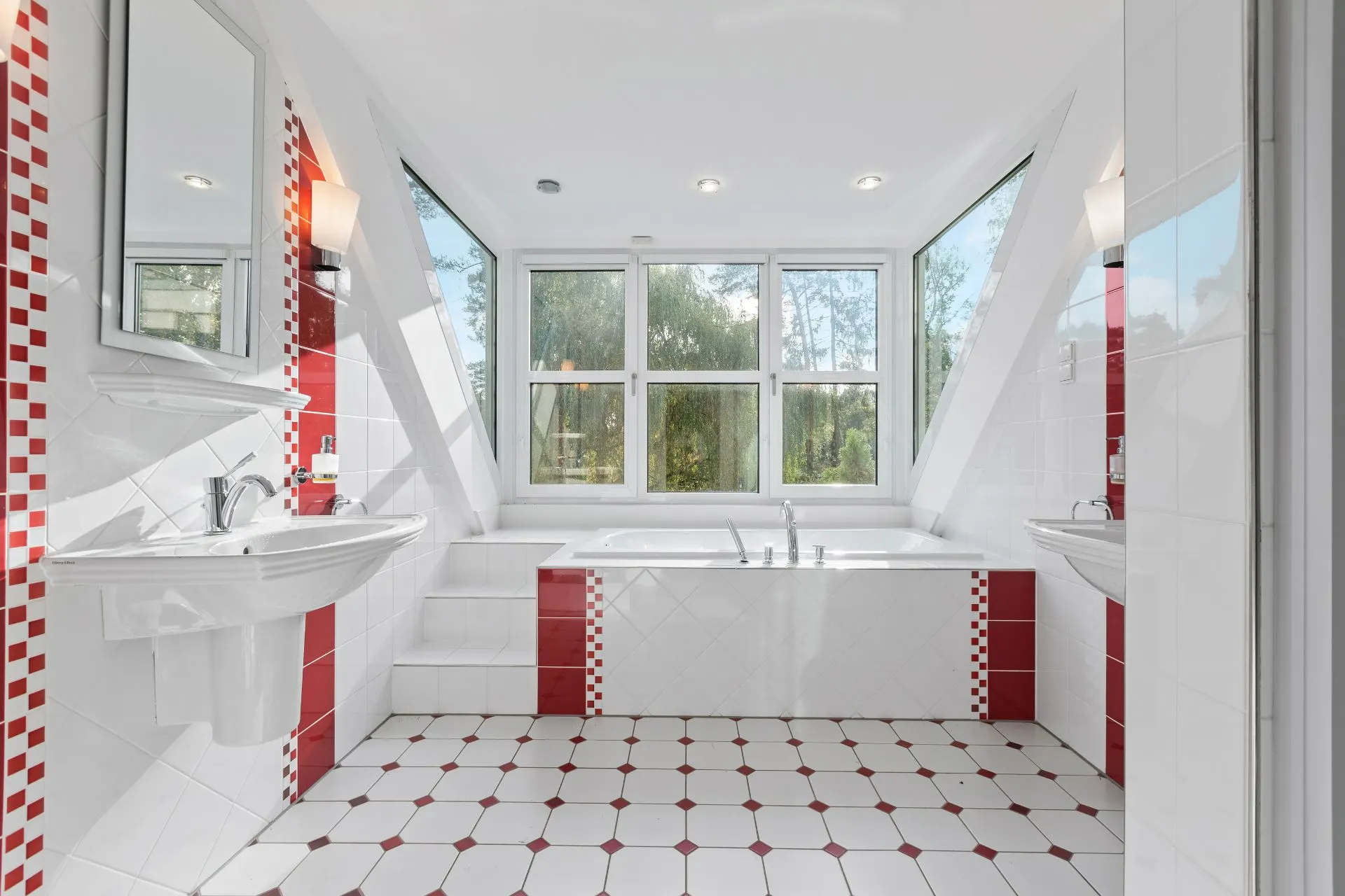 Helles Badezimmer mit großer Badewanne, zwei Waschbecken und roten Fliesenakzenten, Fenster mit Gartenblick.