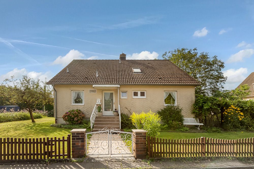 Einfamilienhaus mit Garten, Zaun und kleiner Treppe zum Eingang bei sonnigem Wetter.
