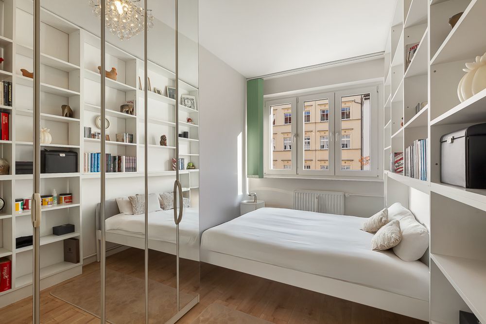 Helles Schlafzimmer mit zwei Betten, Bücherregalen, Spiegel-Schrank und großem Fenster.