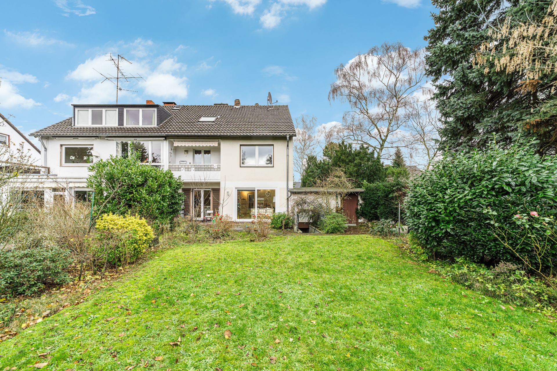 Zweistöckiges Wohnhaus mit großem Garten, Büschen und Bäumen im Vordergrund.