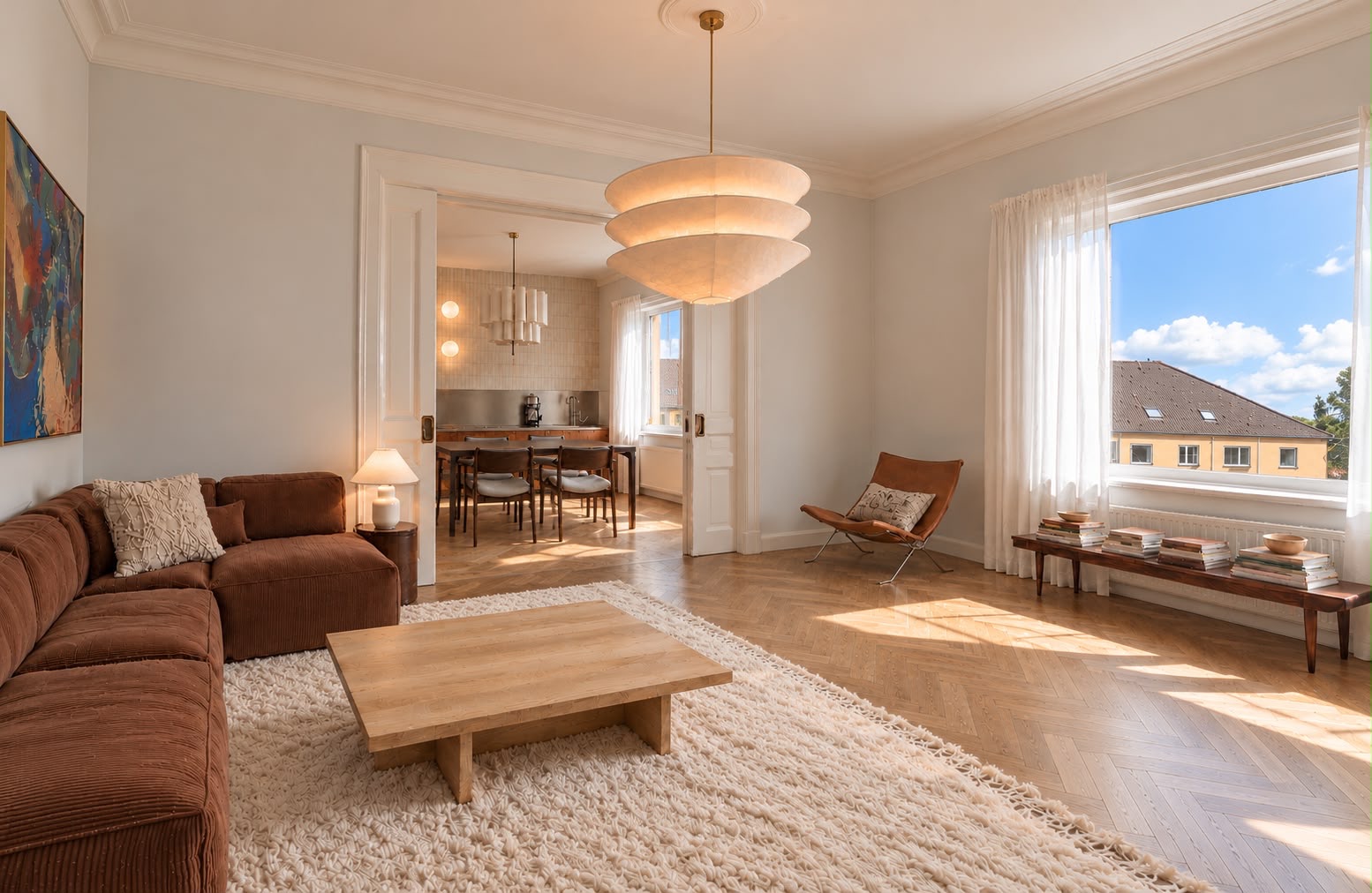 Helles Wohnzimmer mit braunem Sofa, Holztisch, Teppich und großem Fenster, Blick ins Esszimmer.