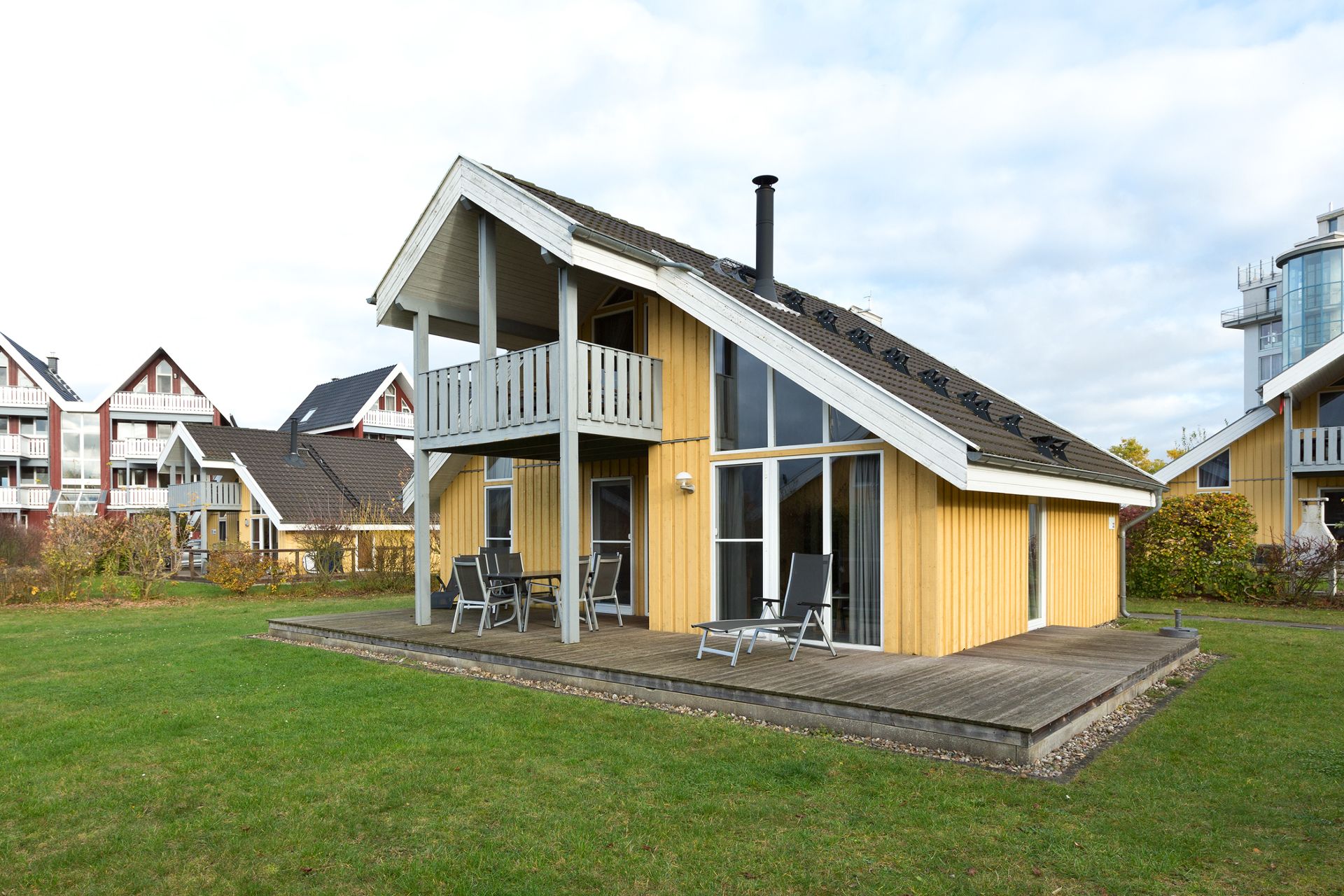 Gelbes Holzhaus mit Balkon, Terrasse und Gartenmöbeln auf einer Rasenfläche.
