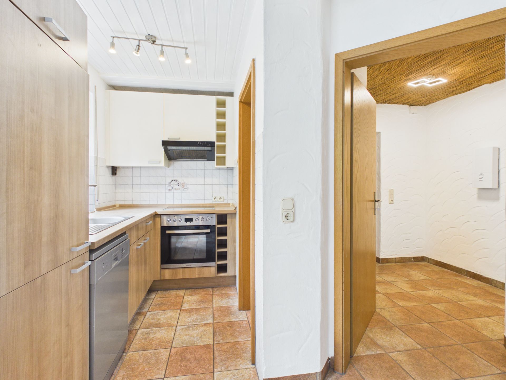 Moderne Küche mit Holzmöbeln und Blick in einen angrenzenden Raum mit Fliesenboden.