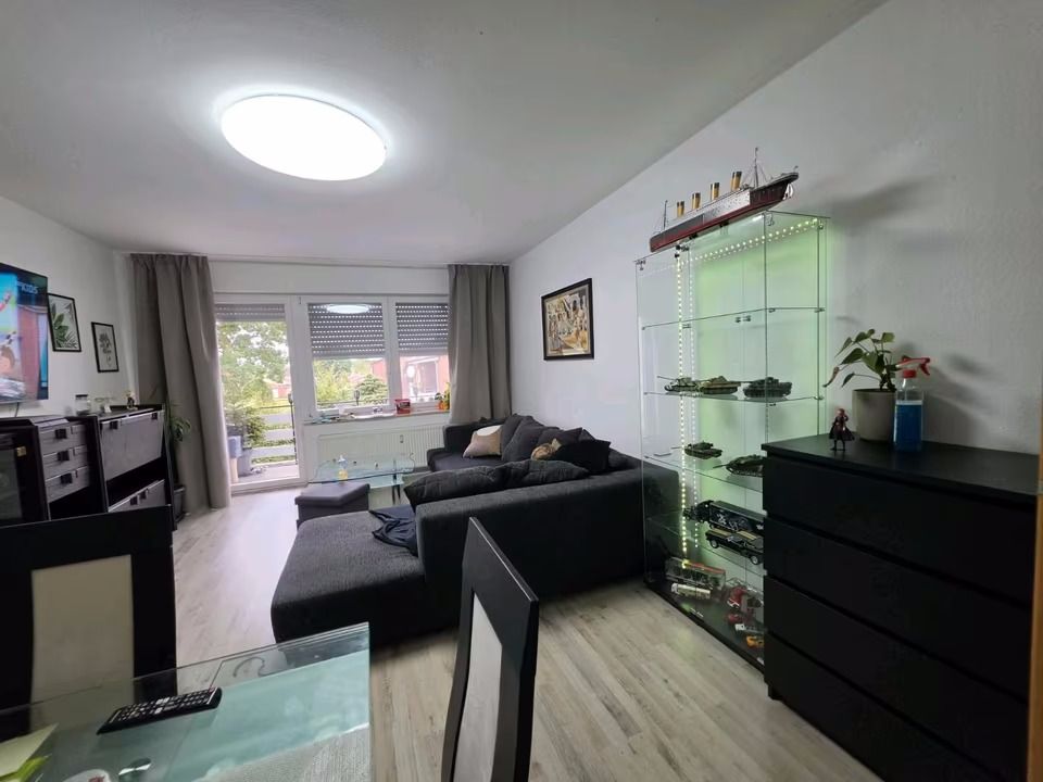 Helles Wohnzimmer mit grauem Sofa, Glasvitrine, Kommode und großen Fenstern.