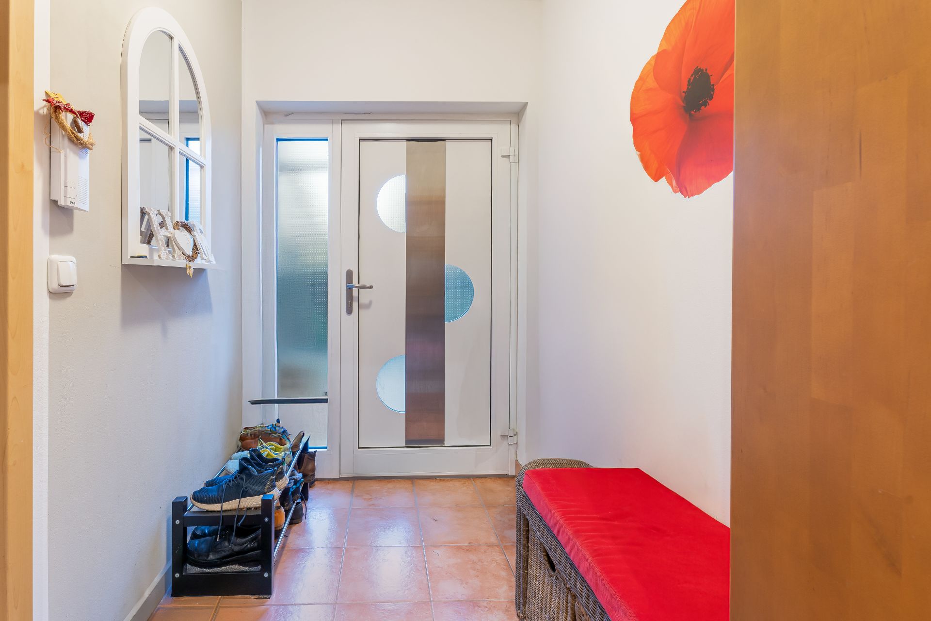 Heller Flur mit Schuhregal, roter Bank, Spiegel und Blumentapete an der Wand.