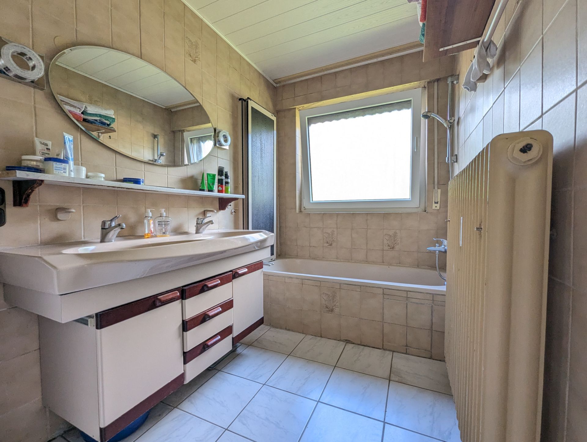 Badezimmer mit Doppelwaschbecken, Badewanne und großem Fenster, beige gefliest.