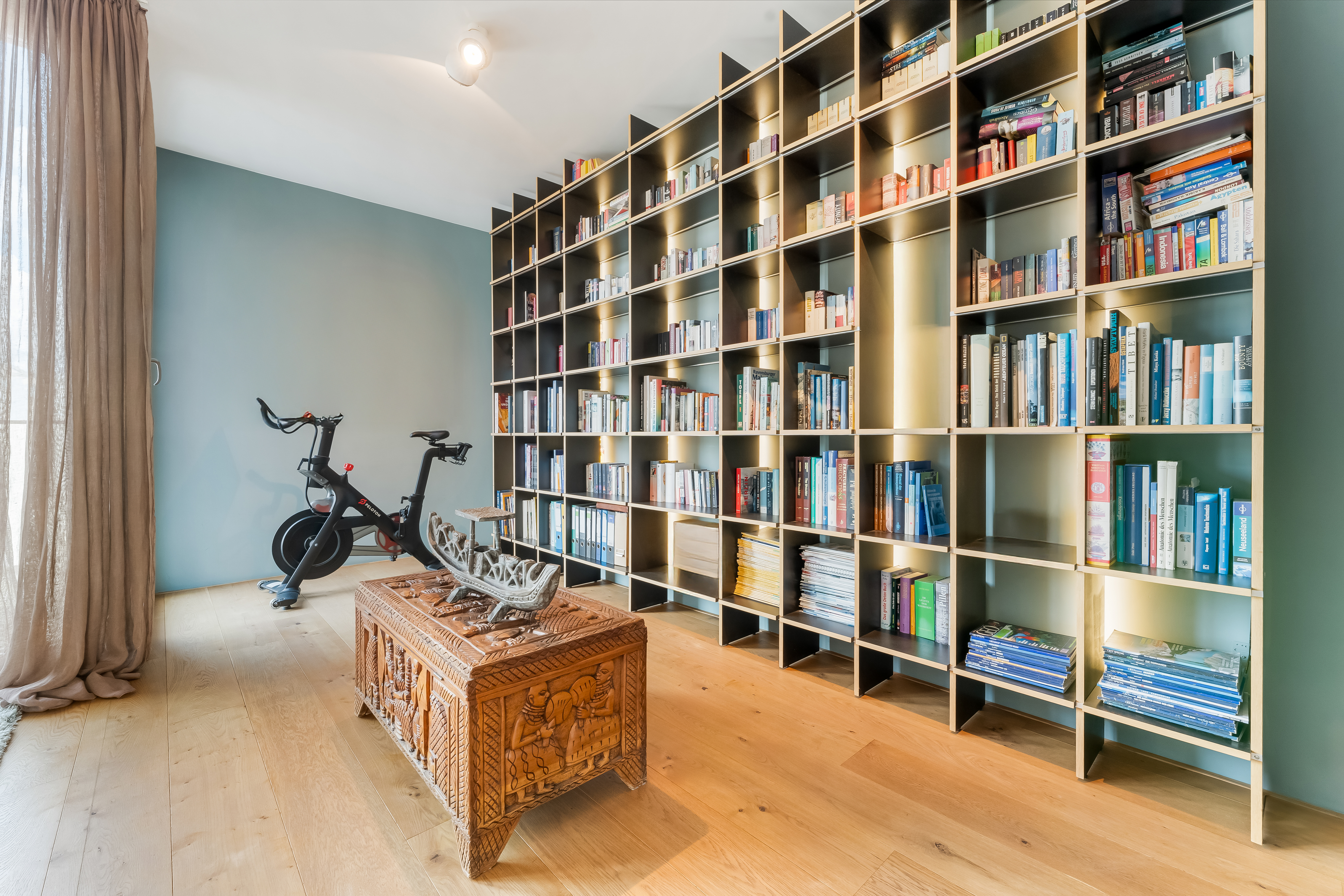 Raum mit großem Bücherregal, Holztisch und einem Heimtrainer auf Holzboden.