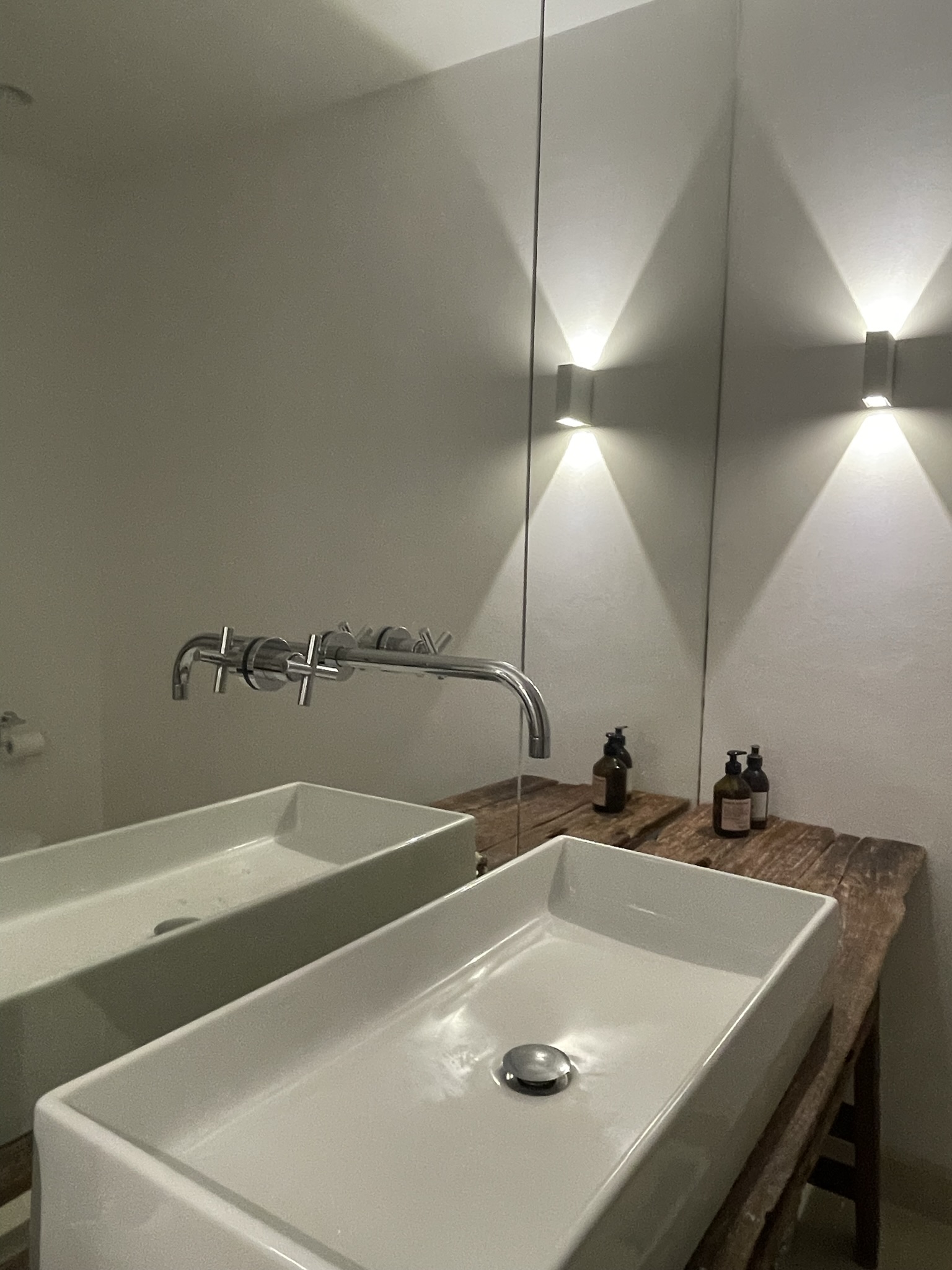 Modernes Badezimmer mit weißem rechteckigem Waschbecken, Wandspiegel und zwei Wandlampen.