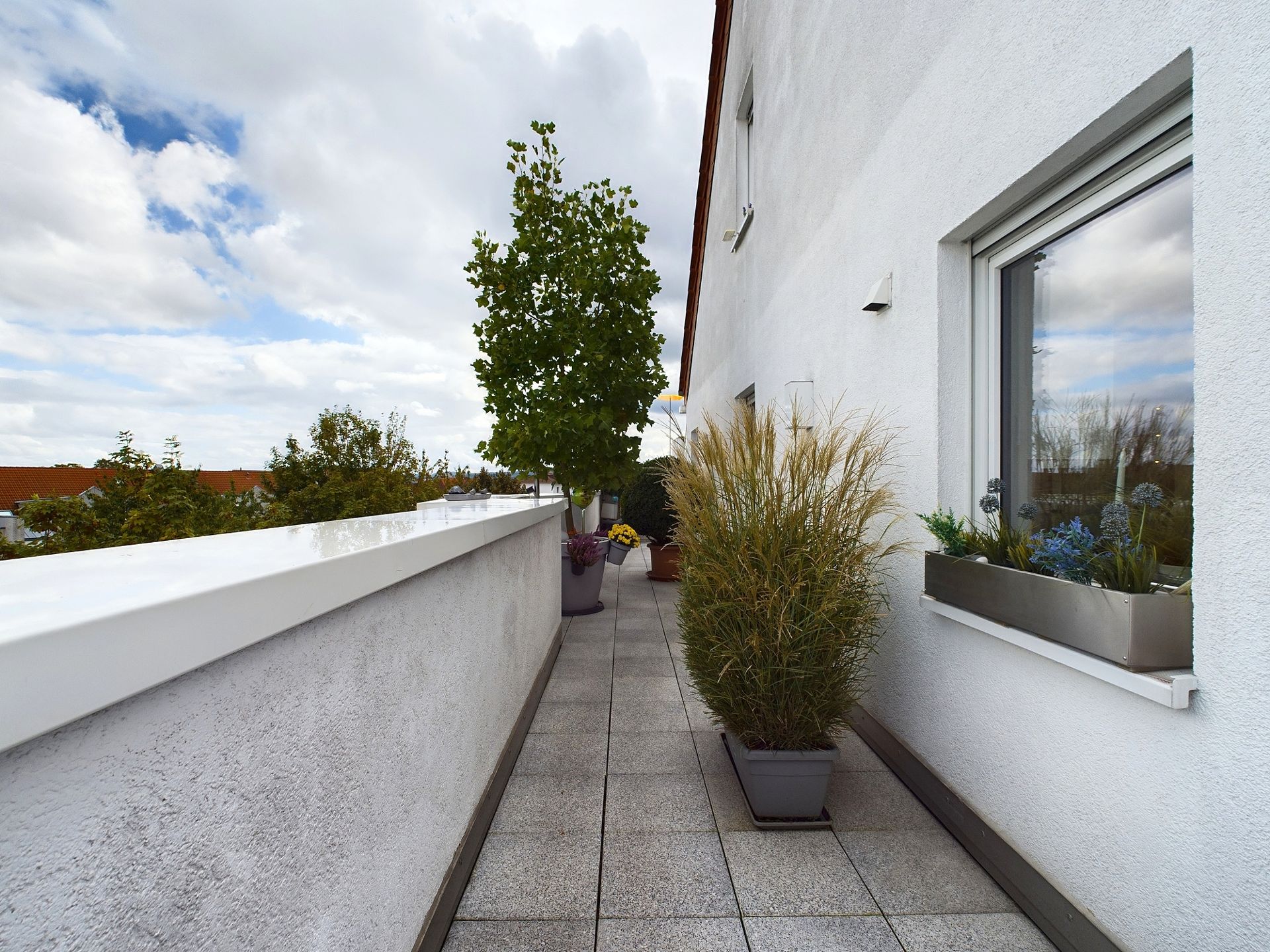 Langer Balkon mit Pflanzkübeln und weißen Wänden an einem Wohngebäude.
