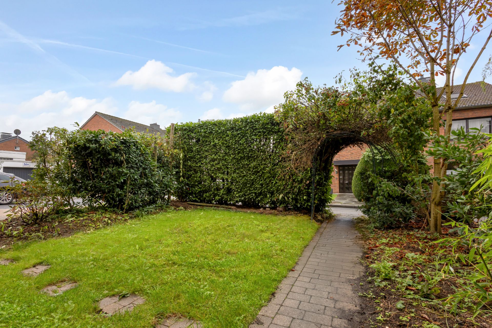 Garten mit Rasenfläche, gepflastertem Weg und grünem Torbogen aus Hecken.