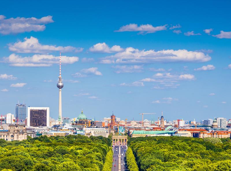Stadtblick mit breiter Straße durch einen grünen Park und Fernsehturm im Hintergrund.