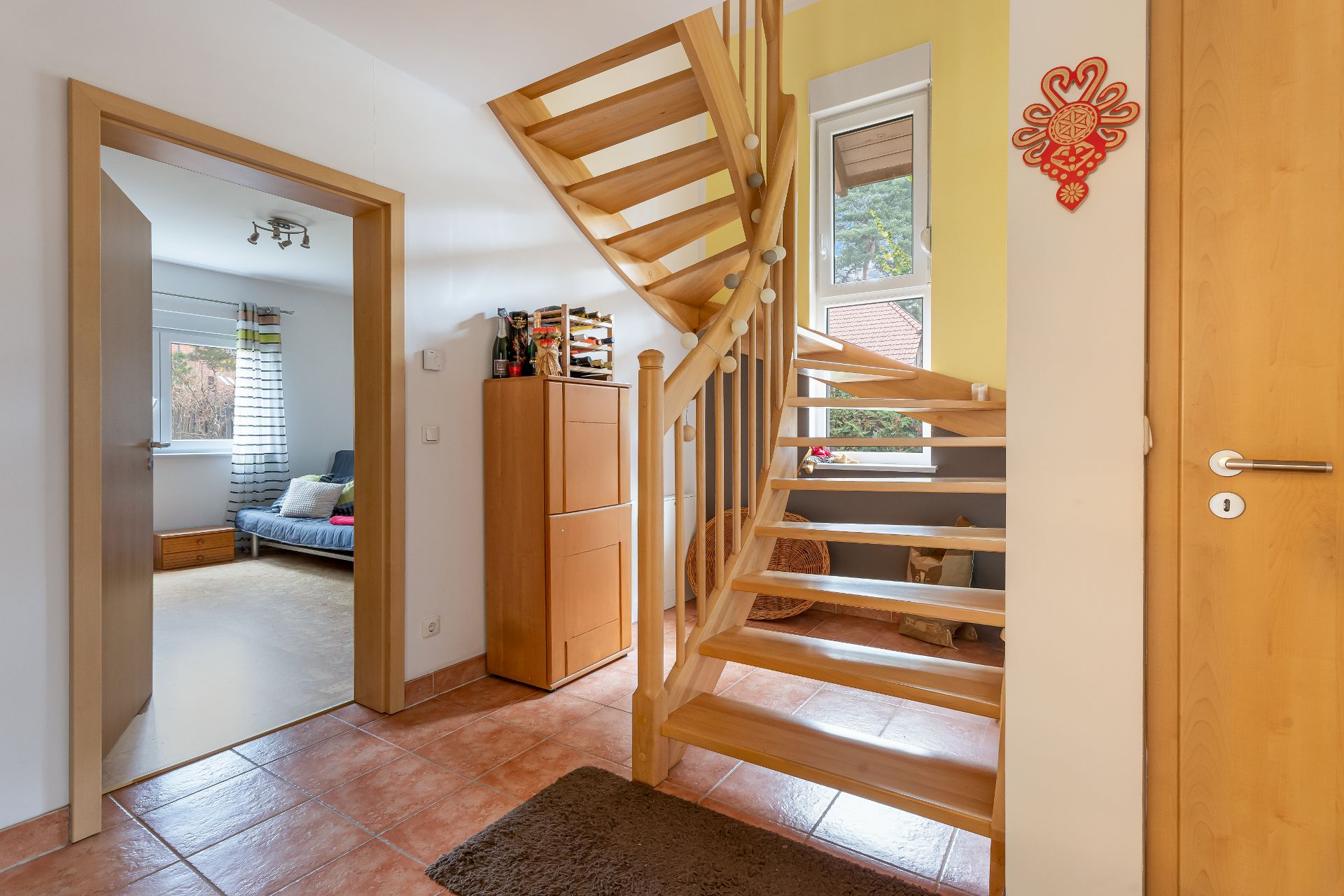 Flur mit Holztreppe, Schrank und offenem Zugang zu einem hellen Zimmer mit Sofa.