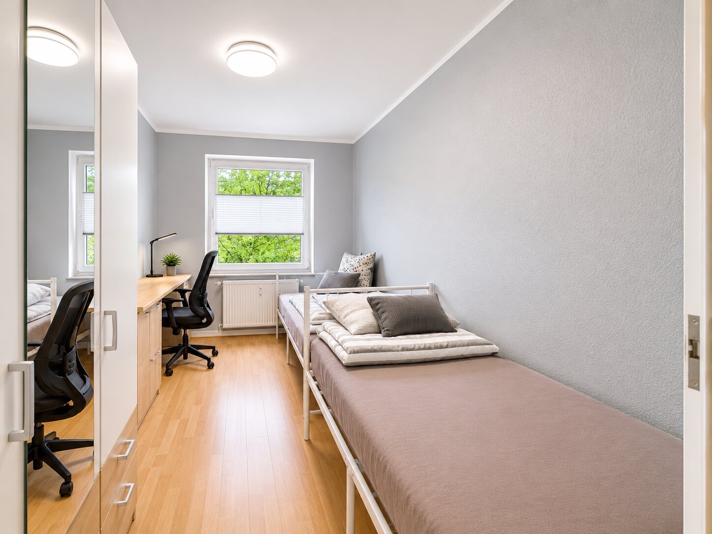 Helles Schlafzimmer mit Einzelbett, Schreibtisch, Stuhl und Kleiderschrank, Fenster mit Blick ins Grüne.