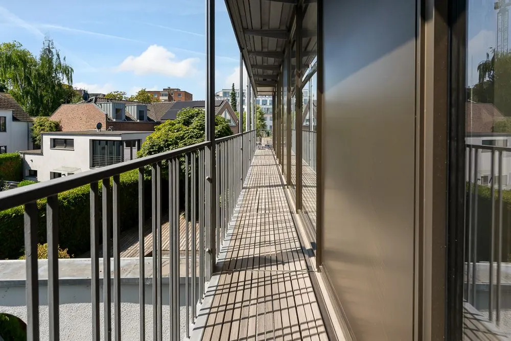 Langer Balkon mit Metallgeländer an einem Wohnhaus, Blick auf Nachbarhäuser und Bäume.