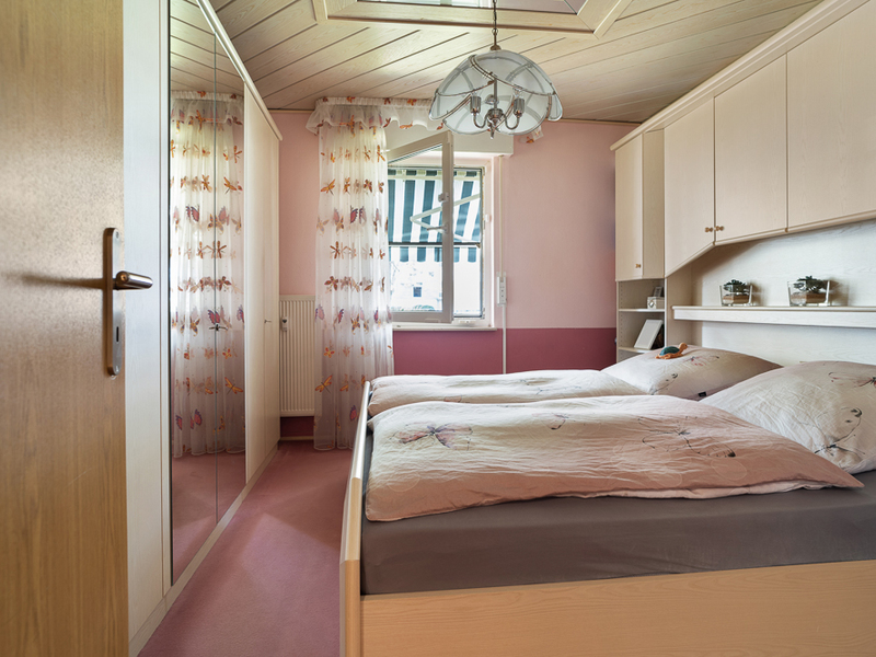 Schlafzimmer mit Doppelbett, Spiegelkleiderschrank und offenem Fenster mit Blumenvorhängen.