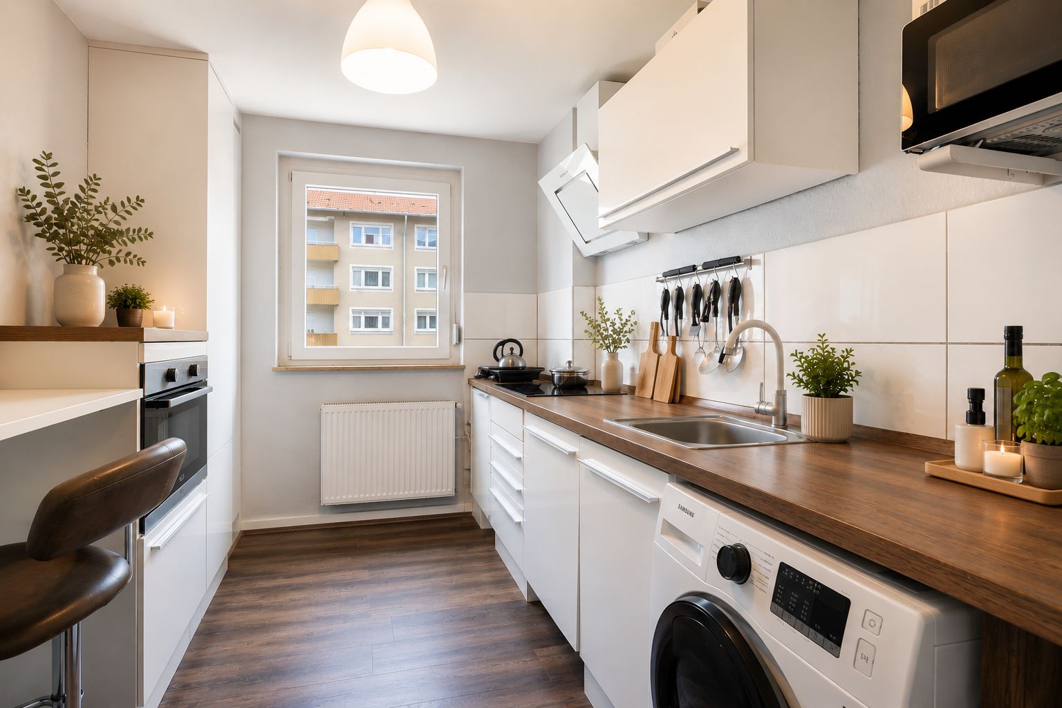 Moderne, schmale Küche mit weißen Schränken, Holzarbeitsplatte und Pflanzen auf der Fensterbank.