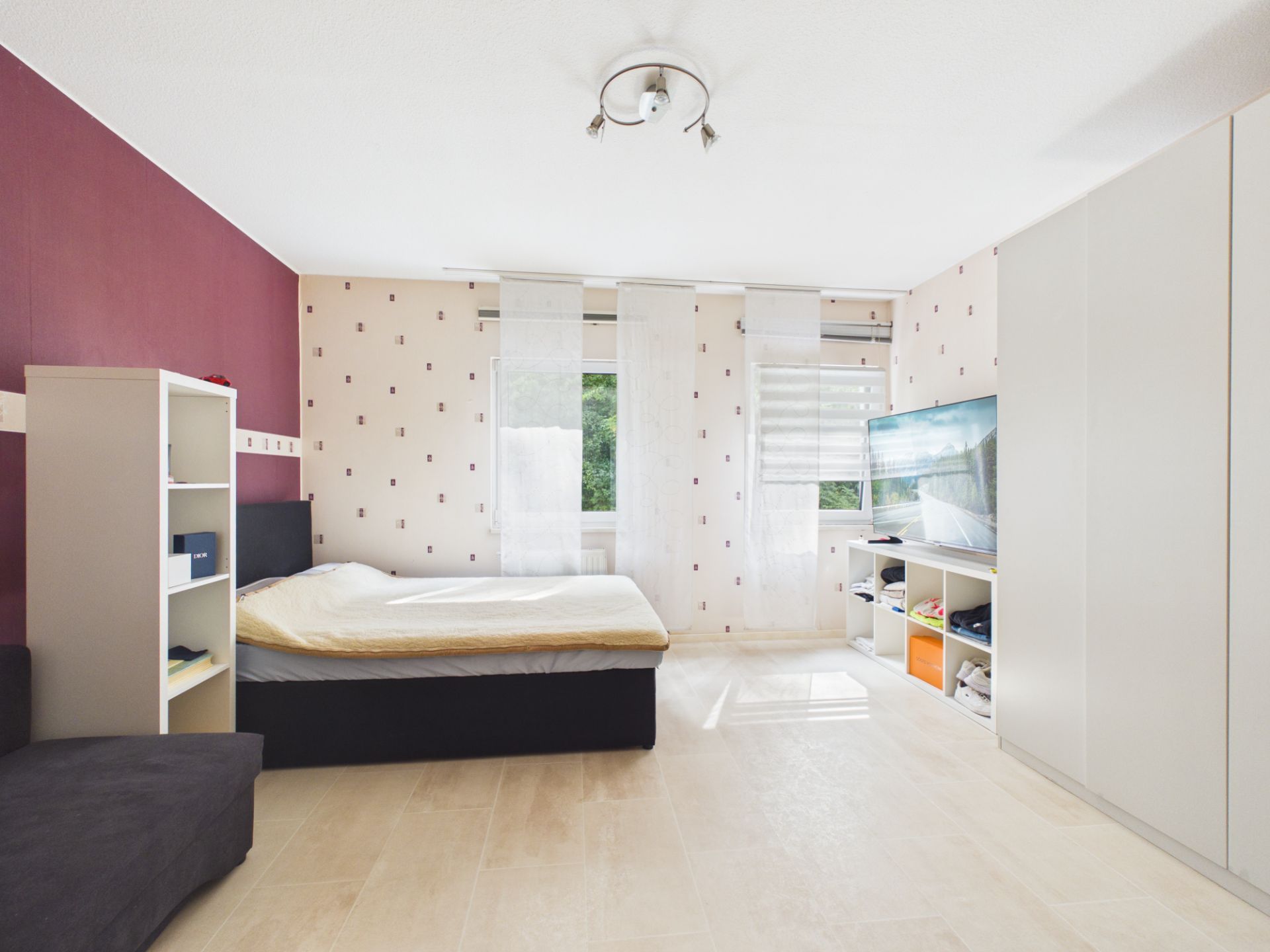 Helles Schlafzimmer mit großem Bett, Regal, Fernseher und Kleiderschrank.