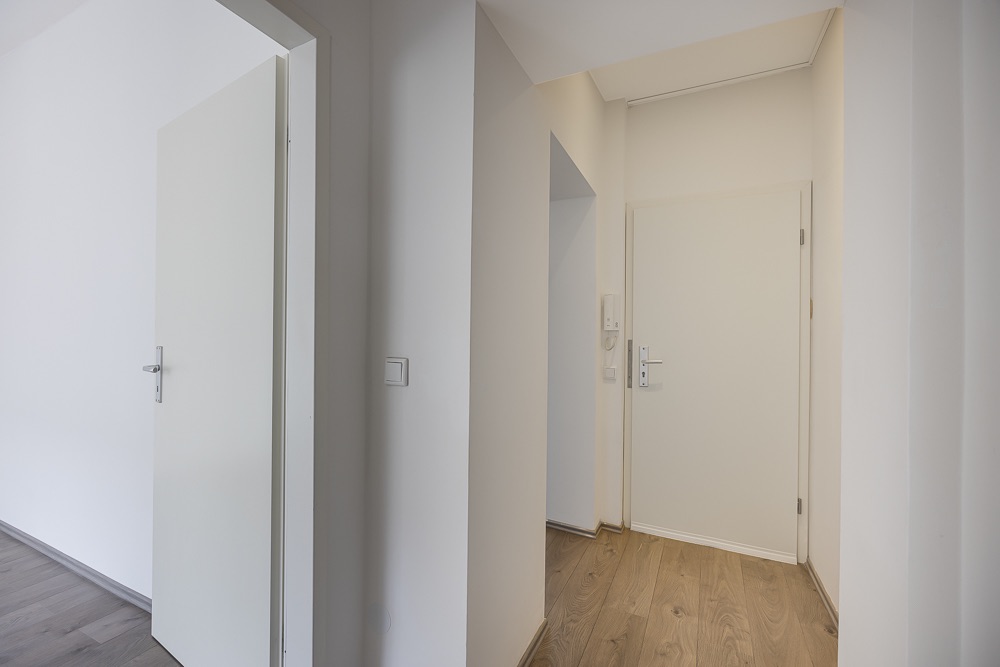 Heller Flur mit Holzboden, weißen Wänden und zwei weißen Türen.