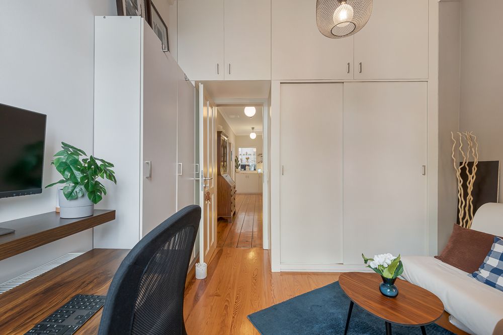 Kleines Wohnzimmer mit Sofa, Schreibtisch, Fernseher, Pflanze und Schrank, Holzboden.
